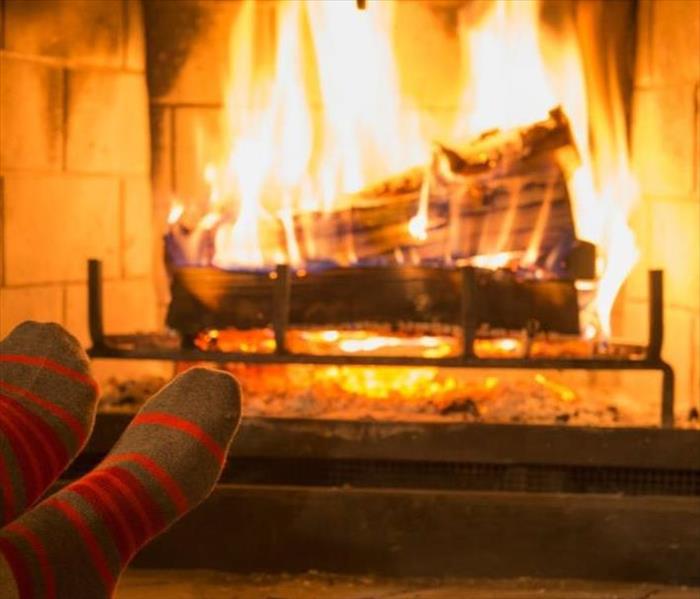A Picture of a lit fireplace with open flames in a living room with a person sitting and their feet propped up to warm them